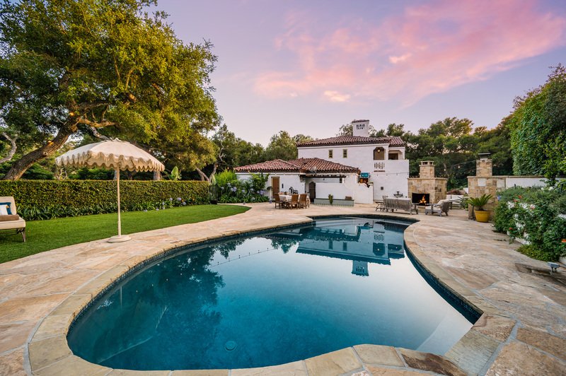 casa con amplia alberca frontal con jardín y una sombrilla
